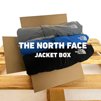 The North Face Jacket Box met drie gestapelde jassen in grijs, blauw en zwart in een geopende verzenddoos op een houten pallet.